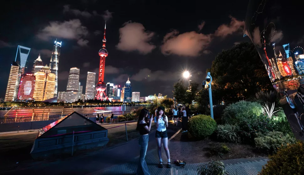 epa11587177 People use their mobile phones on the Bund waterfront area as the city's high-rise buildings are seen illuminated in the background, in central Shanghai, China, 05 September 2024. EPA/ALEX PLAVEVSKI