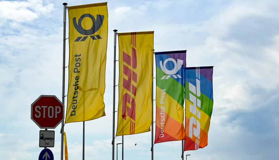 01 June 2022, Brandenburg, Ludwigsfelde: Flags with the logos of Deutsche Post and DHL and flags with these logos on rainbow colors at the Deutsche Post DHL Group mega parcel center in Ludwigsfelde. With a sorting capacity of up to 50,000 items per hour, the parcel center is one of the largest of the total of 37 DHL parcel centers throughout Germany and one of the most efficient in Europe. It is the first mega parcel center with this high sorting capacity in the new federal states. Photo: Jens Kalaene/dpa Photo: Jens Kalaene/DPA