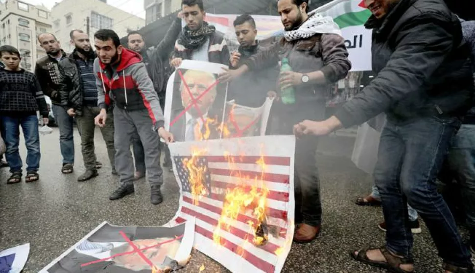 epa06371734 Palestinians burn Israeli and US flags and posters of US President Donald Trump and Israeli Prime Minister Benjamin Netanyahu during protest against the US intention to move its embassy to Jerusalem and to recognize the city of Jerusalem as the capital of Israel, in Rafah, southern Gaza Strip, 06 December 2017. According to media reports, US President Donald J. Trump has informed Palestinian leader Mahmoud Abbas that he intends to recognize Jerusalem as the Israeli capital and will relocate the US embassy from Tel Aviv to Jerusalem. EPA/MOHAMMED SABER