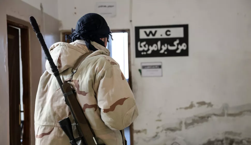 epa11754246 A member of the Syrian opposition stands next to a sign with Persian inscription reading 'Death to America' at a military position allegedly used by Iranian forces after it was captured by the Syrian opposition in the city of Khan Sheikhoun, Idlib countryside, Syria, 03 December 2024. Syrian opposition forces, led by the Islamist militant group Hayat Tahrir al-Sham (HTS), launched an offensive on 27 November, taking large parts of Aleppo, Syria's second-largest city. The offensive triggered counterattacks by the Syrian regime forces as well as Russian and Syrian airstrikes on opposition-controlled areas. EPA/MOHAMMED AL RIFAI