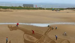 Sand art in EliePeople watch as Jamie Wardley (centre left) and Claire Jamieson (centre right) who are part of the Sand in Your Eye team, draw a violin on Elie Beach in Fife in honour of a 300 year old Stradivarius violin which is on loan to the 2015 East Neuk Festival.Andrew Milligan Photo: Press Association/PIXSELL