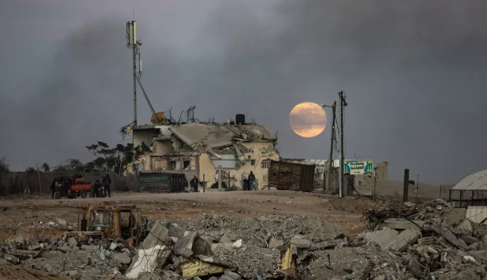 epa11779010 Displaced people walk near destroyed buildings as the full moon rises over Khan Yunis, southern Gaza Strip, 15 December 2024. According to the UN, at least 1.9 million people (or nine in ten people) across the Gaza Strip are internally displaced, including people who have been repeatedly displaced. EPA/HAITHAM IMAD