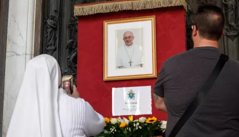 epa12044842 People stand near an image of late Pope Francis at the Basilica of Santa Maria Maggiore in Rome, Italy, 21 April 2025. Pope Francis died on 21 April 2025 at the age of 88, according to the Holy See. Born Jorge Mario Bergoglio in Buenos Aires, Argentina, on 17 December 1936, he was appointed leader of the Catholic Church on 13 March 2013, succeeding Pontiff Emeritus Benedict XVI. EPA/GIUSEPPE LAMI