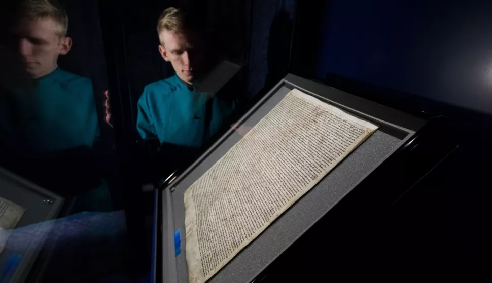 epa07342463 Salisbury Cathedral Verger Tyler Ringwood-Hoare poses next to the 1215 Magna Carta during a photocall at Salisbury Cathedral, in Salisbury in Britain, 04 February 2019. The Magna Carta was returned after three months in storage following an alleged attempted theft. The broken glass case from the original case is exhibited alongside the document as part of its story. EPA/VICKIE FLORES