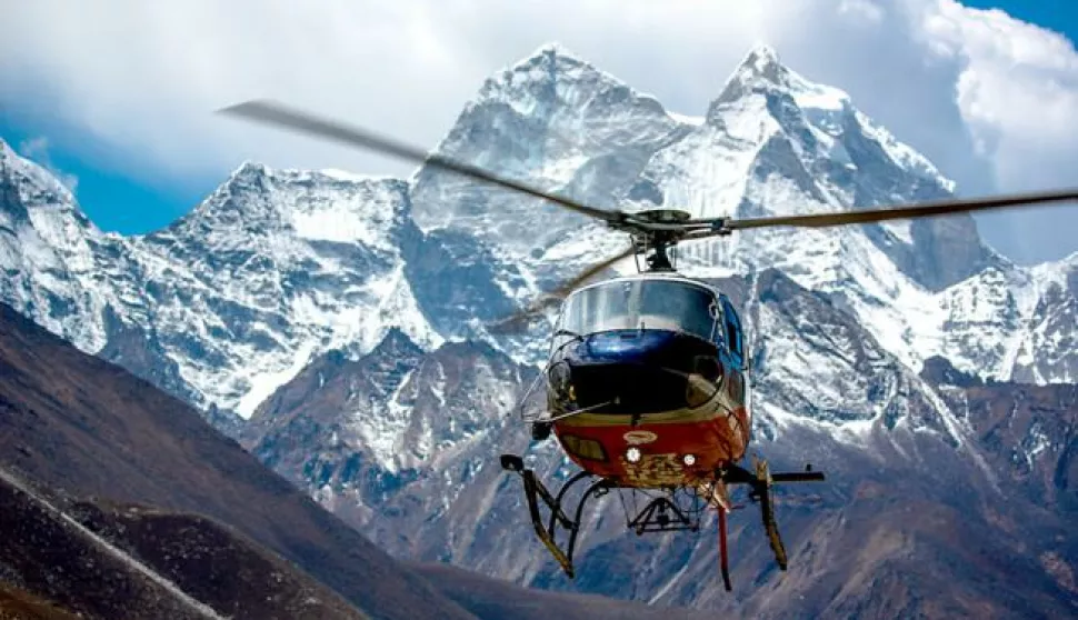A helicopter flies by the mountain with snowy peaks.