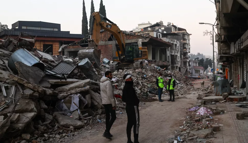 epa10467151 People walk at the site of collapsed buildings after a powerful earthquake, in Hatay, Turkey, 14 February 2023. More than 37,000 people died and thousands more were injured after two major earthquakes struck southern Turkey and northern Syria on 06 February. Authorities fear the death toll will keep climbing as rescuers look for survivors across the region. EPA/SEDAT SUNA