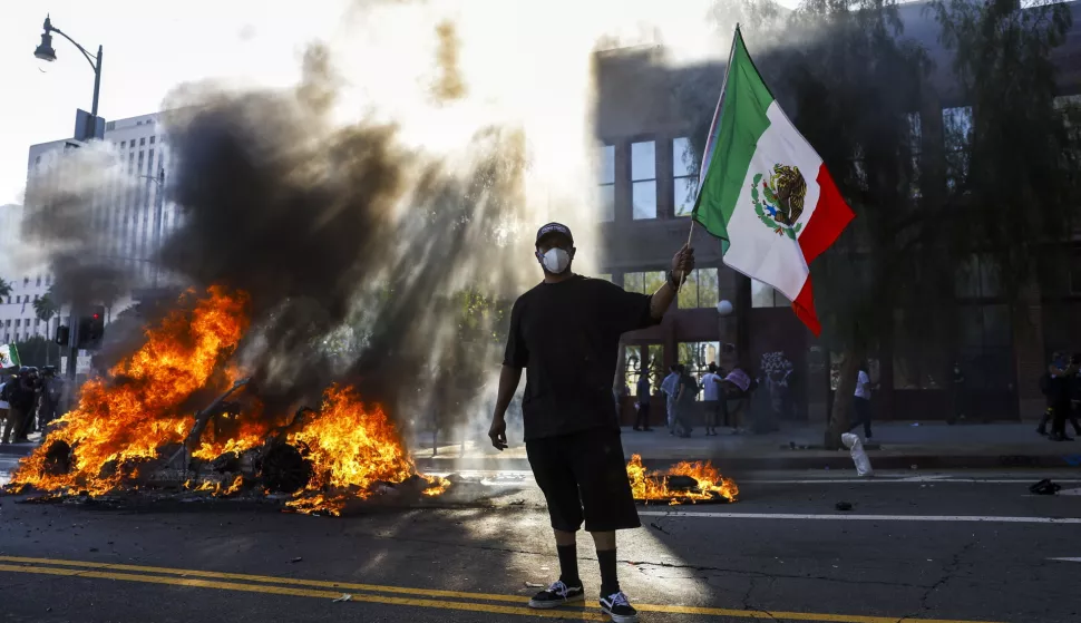epaselect epa12165554 A protester with a Mexican flag looks on as multiple cars burn during immigration raid protests in Los Angeles, California, USA, 08 June 2025. US President Donald Trump has deployed 2,000 National Guard troops, despite not receiving a request from the state of California for any additional assistance, following large protests against ongoing immigration enforcement raids in the Los Angeles area over the last couple of days. EPA/CAROLINE BREHMAN