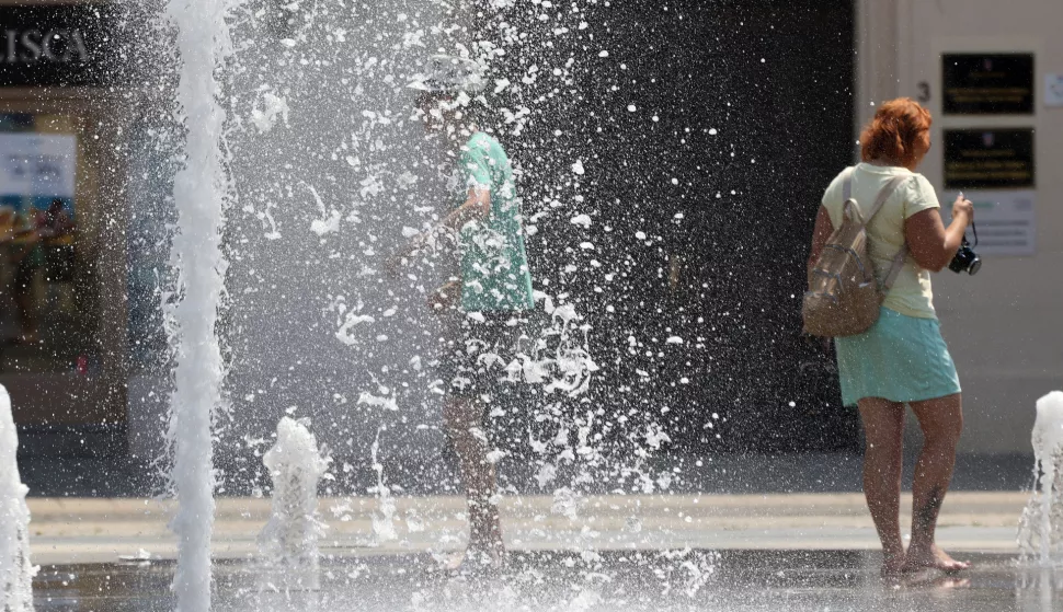 Osijek, 12. 07. 2024, Trg Ante Starcevica, fontana, turisti se osvjezavaju u fontani. Oko 14 sati temperatura u Osijeku je bila 38,8 C tako je pokazivao led displej na obali Drave u Zimskoj luci. Ljudi se snalaze na razne nacine kako bi se zastitili od vrucine i sunca. snimio GOJKO MITIĆ