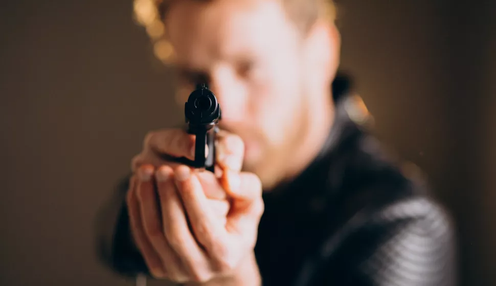 Handsome man actor posing in studio with weaponilustracija, crna kronika, kriminal, kriminalac, pravosuđe, ubojstvo, smrt, pištolj, oružjefreepik 