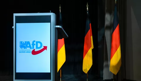 23 May 2025, Saxony-Anhalt, Magdeburg: The AfD logo on the lectern with German flags in the background on the stage in the assembly hall. The candidates for the 2026 state election are being nominated. Photo: Heiko Rebsch/dpa Photo: Heiko Rebsch/DPA