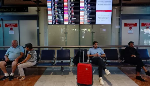 epa10187695 People sit next to a flight information board at Nice Cote d'Azur airport, in Nice, France, 16 September 2022. Several flights are canceled due to a strike by air traffic controllers in France. EPA/SEBASTIEN NOGIER