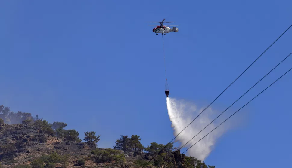 epa12212223 A firefighting helicopter attempts to extinguish scattered blazes burning in the forest during a wildfire in Ierapetra, on Crete island, Greece, 03 July 2025. According to Fire Department spokesperson Chief Vasilios Vathrakoyannis, 230 firefighters with 13 foot teams, 46 vehicles, and 10 helicopters are battling multiple wildfire outbreaks in Ierapetra, Crete, after the fire broke out on the afternoon of 02 July. Strong winds reaching 9 Beaufort continue to spark new blazes and smog, complicating efforts. Water tankers and machinery from Crete, Central Macedonia, and the General Staff of National Defense are also assisting. EPA/NIKOS CHALKIADAKIS