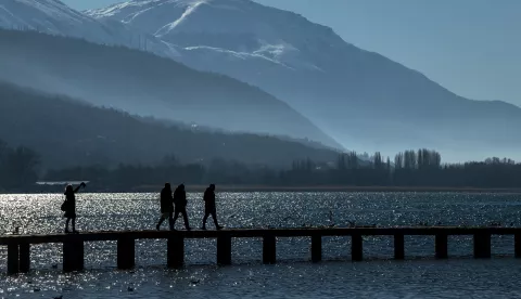 epa11076262 People walk over a wooden bridge at Ohrid Lake on a very cold and sunny day in Ohrid, Republic of North Macedonia, 14 January 2024. A cold wave struck North Macedonia recently, but the sunny weather allowed locals and foreign tourists to enjoy Lake Ohrid despite morning temperatures dropping to -8 degrees Celsius. EPA/GEORGI LICOVSKI