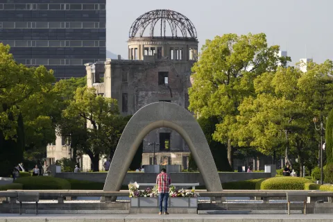 epa10633543 A man offers prayers in front of a cenotaph as the Atomic Bomb Dome is seen in the background at Hiroshima Peace Memorial Park in Hiroshima, western Japan, 17 May 2023. The G7 Hiroshima Summit will be held from 19 to 21 May 2023. EPA/FRANCK ROBICHON
