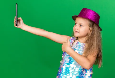 smiling little blonde girl with purple party hat thumbing up taking selfie on phone isolated on green background with copy spaceIako dru&scaron;tvene mreže omogućuju povezivanje, izražavanje i informiranost, sve je vi&scaron;e pokazatelja da njihova pretjerana uporaba dovodi do emocionalnih te&scaron;koća, gubitka samopouzdanja, zavisti, kroničnog uspoređivanja s drugima te raznih rizičnih oblika pona&scaron;anja, tvrde u Psiholo&scaron;kom centru, dodajući kako su sadržaji kojima su mladi izloženi na dru&scaron;tvenim mrežamau vrlo često dorađeni, nerealni i orijentirani na stvaranje dojma savr&scaron;enstvafreepik