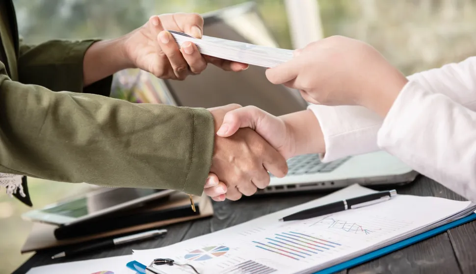 Business people shaking hands, finishing up meeting. businessman giving money to his partner while making contract - bribery and corruption concepts.banka novac kredit ilustracija freepik
