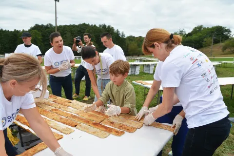 Ozalj, 06.09. 2025. - Jaškovo u općini Ozalj danas se po drugi puta upisalo u Guinnessovu knjigu svjetskih rekorda, složenom štrudlom od jabuke ukupne dužine 3.136 metara, koja je sastavljena od 8.940 komada štrudle. Sve je to bilo postavljeno na stolove u obliku dvostruke šesterokrake zvijezde, tlocrta tvrđave na kojoj se razvio Karlovac. Rekord je verificirala Guinnesova sutkinja Paulina Sapinska. Na fotografiji i male ruke su pomogle u slaganju štrudle. foto HINA/ Mladen VOLARIĆ/ mv