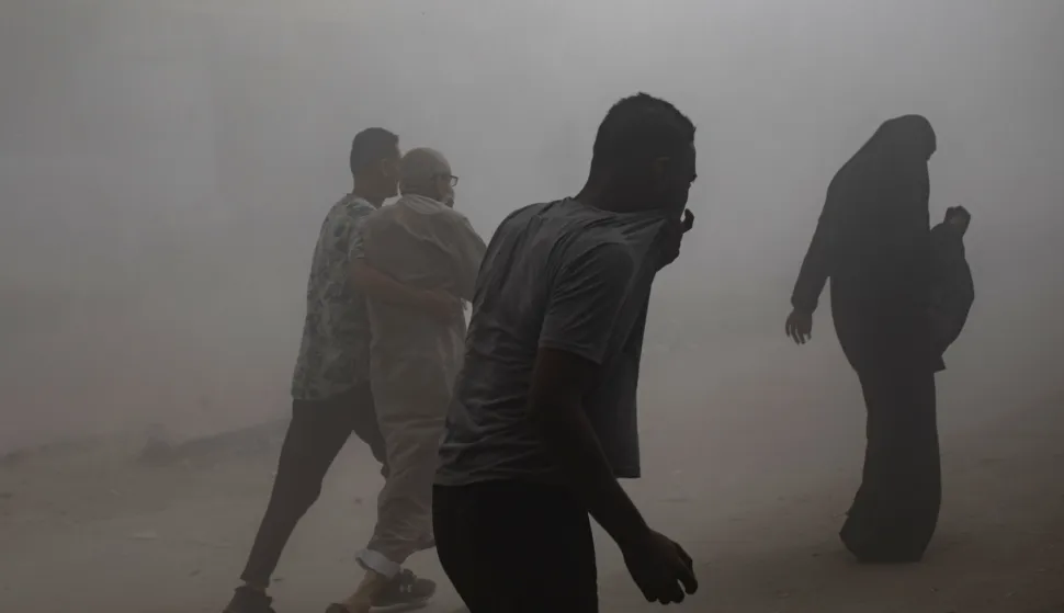 epa12380197 People walk as smoke and dust fill the air after the Al-Ghafari residential tower was hit by an Israeli airstrike in Gaza City, 15 September 2025. More than 64,900 Palestinians have been killed in the Gaza Strip since October 2023, according to the Palestinian Ministry of Health. EPA/HAITHAM IMAD