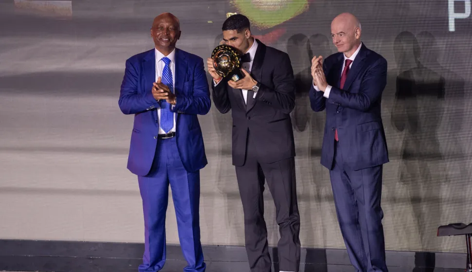 epa12536619 Morocco's Achraf Hakimi (C), stands with CAF President Patrice Motsepe (L), and FIFA President, Gianni Infantino, (R), after receiving the 2025 CAF African Footballer award during the 2025 Confederation of African Football (CAF) Awards in Sale, Morocco, 19 November 2025. The CAF Awards celebrates the exceptional performances of African footballers, coaches, and teams over the past year. EPA/JALAL MORCHIDI