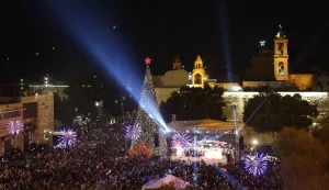 epa12575242 People gahter during the lighting of the Christmas tree ceremony at the Manger Square, next to the Church of Nativity in the background, in the West Bank city of Bethlehem, 06 December 2025. EPA/ATEF SAFADI