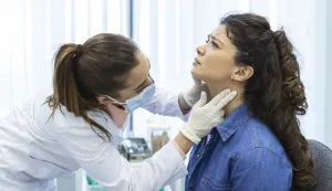 Endocrinologist examining throat of young woman in clinic. Women with thyroid gland test. Endocrinology, hormones and treatment. Inflammation of the sore throat