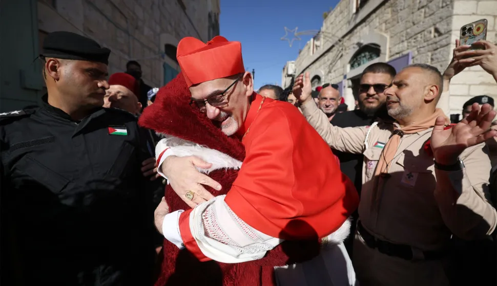 Latin Patriarch of Jerusalem Italian Pierbattista Pizzaballa hugs a man dressed up as Santa Claus as he is welcomed by pilgrims, tourists and Palestinians upon arrival to lead the Christmas Mass in the Church of the Nativity in the Israeli-occupied West Bank city of Bethlehem, believed to be the birthplace of Jesus Christ, on December 24, 2025. Palestinian Scouts marched under a clear blue sky in Bethlehem on December 24, 2025, as the Palestinian city emerged from the shadow of the war in Gaza to celebrate its first festive Christmas in more than two years. Throughout the Gaza war that began with Hamas's attack on Israel in October 2023, a sombre tone marked Chistmases in Bethlehem, the biblical birthplace of Jesus Christ. (Photo by HAZEM BADER/AFP)