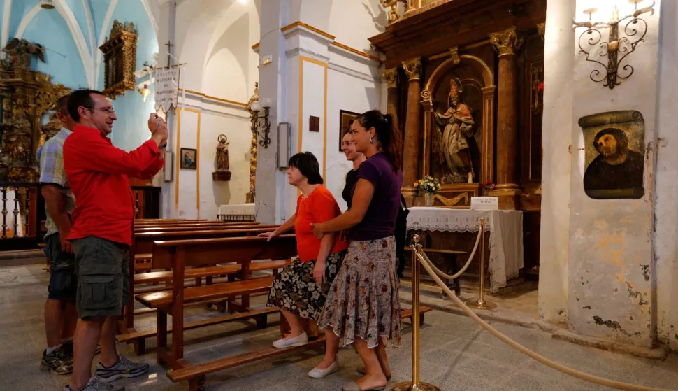 (FILES) People take pictures of the deteriorated version of "Ecce Homo" by 19th-century painter Elias Garcia Martinez, after its restoration by Cecilia Gimenez, 81, at the Borja Church in Zaragoza on August 28, 2012. The Spanish woman whose failed restoration of a century-old painting of Jesus Christ captured global headlines more than a decade ago has died at 94. Cecilia Gimenez rose to international fame in 2012 after her botched restoration of the Ecce Homo fresco at a church in Borja, northeastern Spain, drew worldwide media attention. (Photo by CESAR MANSO/AFP)