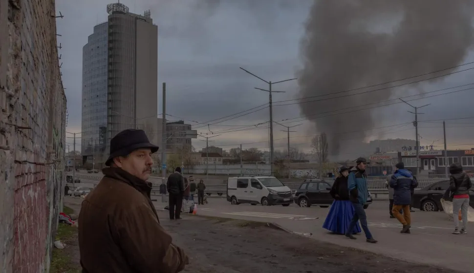 AFP PICTURES OF THE YEAR 2025Pedestrians walk at a flea market as smoke rises in the distance following the Russian missile attack, in Kyiv on April 6, 2025, amid the Russian invasion of Ukraine.. Kyiv Mayor said the city was under missile attack on April 6, 2025 with explosions in the Ukrainian capital, two days after a Russian missile killed 18 people in Ukraine's President's hometown. (Photo by Roman PILIPEY/AFP)/AFP PICTURES OF THE YEAR 2025