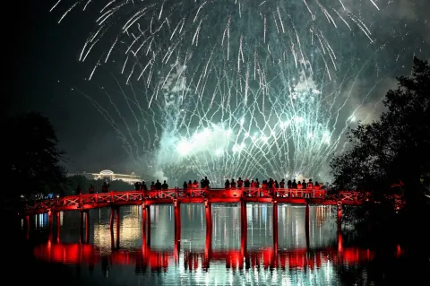 Revellers watch the New Year's Eve fireworks from the The Huc Bridge at Hoan Kiem Lake in Hanoi on January 1, 2026. (Photo by Nhac NGUYEN/AFP)