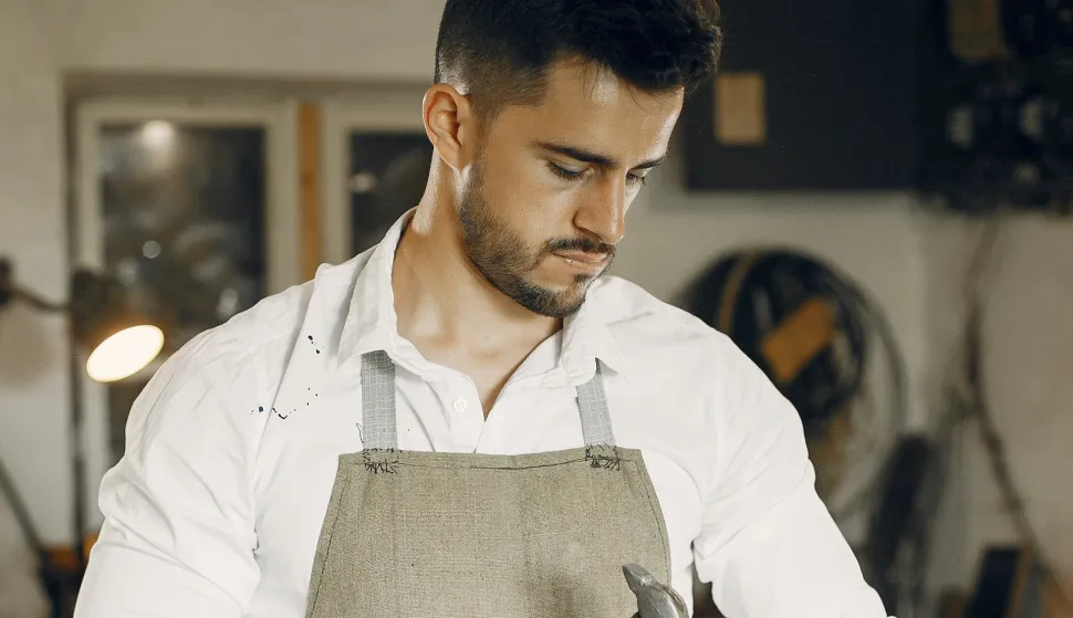 Man working with a wood. Carpenter in a white shirt. Man with a chisel and a hammer