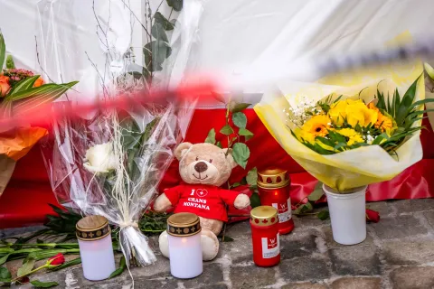 This photograph shows flowers, candles and a teddy bear laid near the site of a fire that ripped through a bar during New Year's Eve celebrations in the Alpine ski resort town of Crans-Montana killing around 40 people and injuring more than 100 others, in Crans-Montana on January 2, 2026. Investigators raced on January 2, 2026 to identify the victims of a fire that ripped through a bar in the Swiss Alps town of Crans-Montana, turning a New Year's celebration into one of the country's worst tragedies. Frederic Gisler, police commander in the Wallis canton in southwestern Switzerland, told reporters that authorities had counted "around 40 people who have died and around 115 injured, most of them seriously". (Photo by MAXIME SCHMID/AFP)