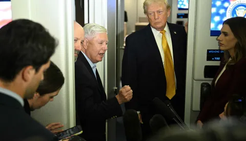 US senator Lindsey Graham (C), Republican of South Carolina, flanked by President Donald Trump (R) and the Secretary of Commerce Howard Lutnick, speaks with reporters aboard Air Force One on their way back to Washington, DC, on January 4, 2026. President Trump is returning to DC after spending the holidays at his Mar-a-Lago residence in Palm Beach, Florida. (Photo by Jim WATSON/AFP)