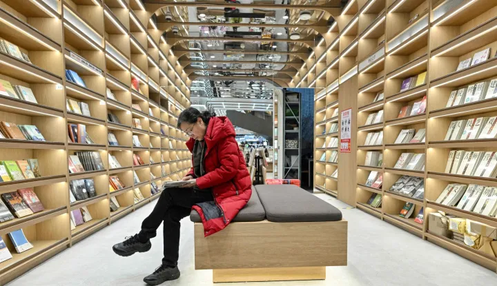 This picture taken on December 18, 2025 shows a woman reading a book at a bookstore in Beijing. Sales of hard-copy books across the country have failed to bounce back to pre-pandemic levels, data shows, despite authorities' efforts to boost domestic consumption and an e-commerce boom.Yet in recent years the number of physical bookshops has "maintained steady growth", the head of a publishing industry group said January 2025. (Photo by Adek BERRY/AFP)/TO GO WITH China-social-books-architecture by Mary YANG