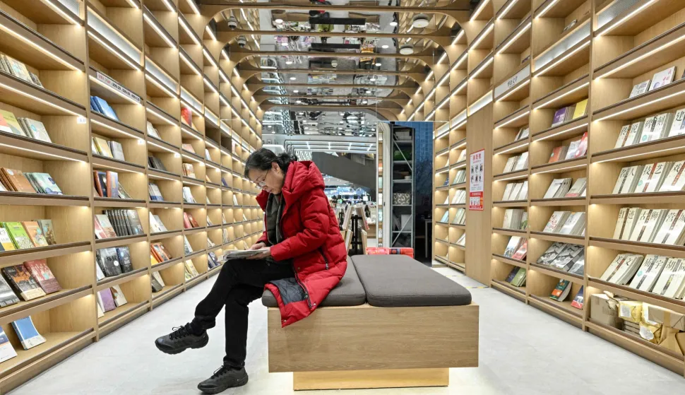 This picture taken on December 18, 2025 shows a woman reading a book at a bookstore in Beijing. Sales of hard-copy books across the country have failed to bounce back to pre-pandemic levels, data shows, despite authorities' efforts to boost domestic consumption and an e-commerce boom.Yet in recent years the number of physical bookshops has "maintained steady growth", the head of a publishing industry group said January 2025. (Photo by Adek BERRY/AFP)/TO GO WITH China-social-books-architecture by Mary YANG