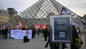 (FILES) A notice informs members of the public of the closure of the Louvre Museum as members of the French CGT union protest outside the entrance as museum workers voted to go on strike against increasingly deteriorating working conditions and the declining visitor experience at the world famous museum, in Paris on December 15, 2025. The Louvre museum was forced to close on January 12, 2026 after its staff, who have been on strike since mid-December in a bid to secure better working conditions, decided to continue their action, AFP learned from the museum and trade unions. (Photo by Blanca CRUZ/AFP)