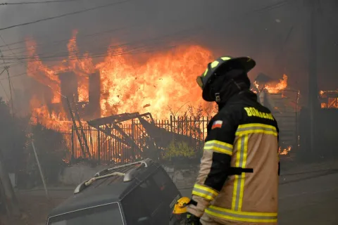 Firefighters try to extinguish a burning house during a wildfire in Concepcion, Chile, on January 18, 2026. Chilean President Gabriel Boric declared a state of emergency on January 18 for two southern regions where raging wildfires have forced about 20,000 people to evacuate their homes. (Photo by GUILLERMO SALGADO/AFP)
