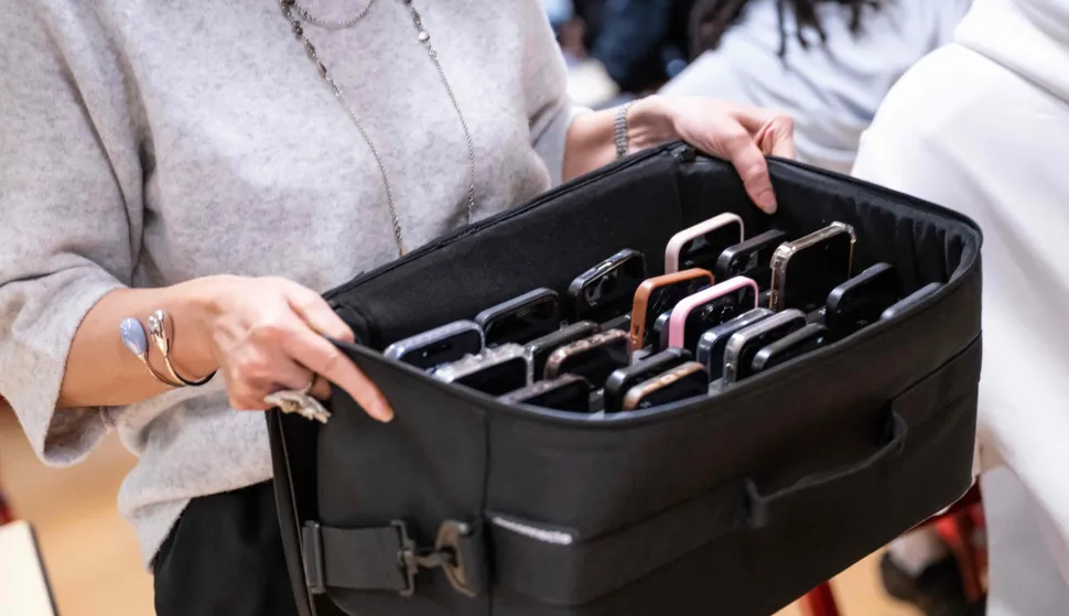 A teacher holds a suitcase containing students' mobile phones, set aside during classes at the Jean Mermoz vocational high school in Montsoult, in the northern suburbs of Paris, on January 14, 2026. According to a bill that is soon to be debated in Parliament, the government wants to ban the use of cell phones in high schools, as well as social media for children under 15. (Photo by BERTRAND GUAY/AFP)