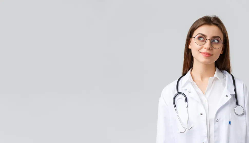 Healthcare workers, medicine, insurance and covid-19 pandemic concept. Dreamy young talented doctor in white scrubs and glasses, looking upper left corner thoughtful and smiling, imaging something.