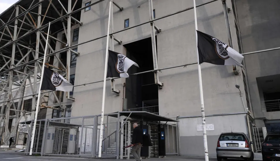 A pedestrian walks past the Toumba stadium also known as the PAOK stadium with its' flags flying at half mast in Thessaloniki on January 27, 2026, following the fatal collision of a minibus transporting Greek football fans with a truck in Romania. A minibus transporting Greek football fans collided with a truck in Romania on January 27, 2026, leaving seven dead and three injured, officials said. The minibus carrying 10 men was travelling from Greece to France where the fans were planning to attend the Europa League match between PAOK and Lyon on January 29, 2026, when it collided with a truck in Timis county in western Romania, local police said. (Photo by Sakis Mitrolidis/AFP)