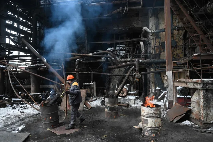 An employee stokes a fire in a barrel at a power plant of Ukrainian energy provider DTEK, which was heavily damaged during air attacks, at an undisclosed location on January 23, 2026, amid the Russian invasion of Ukraine. (Photo by YURIY DYACHYSHYN/AFP)
