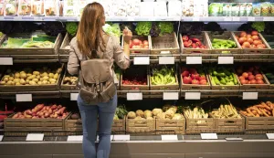 Good looking woman standing in front of vegetable shelves choosing what to buy.trgovina kupnja voće povrće