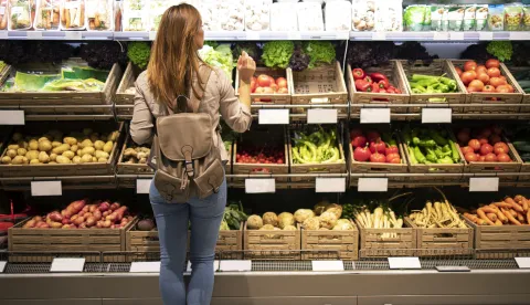 Good looking woman standing in front of vegetable shelves choosing what to buy.trgovina kupnja voće povrće