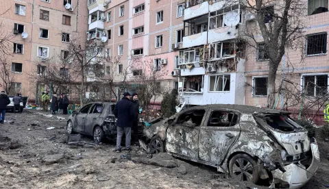 People stand next to burned cars and a damaged residential building in an area hit by an air attack in a residential neighborhood in Zaporizhzhia on January 28, 2026, amid the Russian invasion of Ukraine. (Photo by Darya NAZAROVA/AFP)