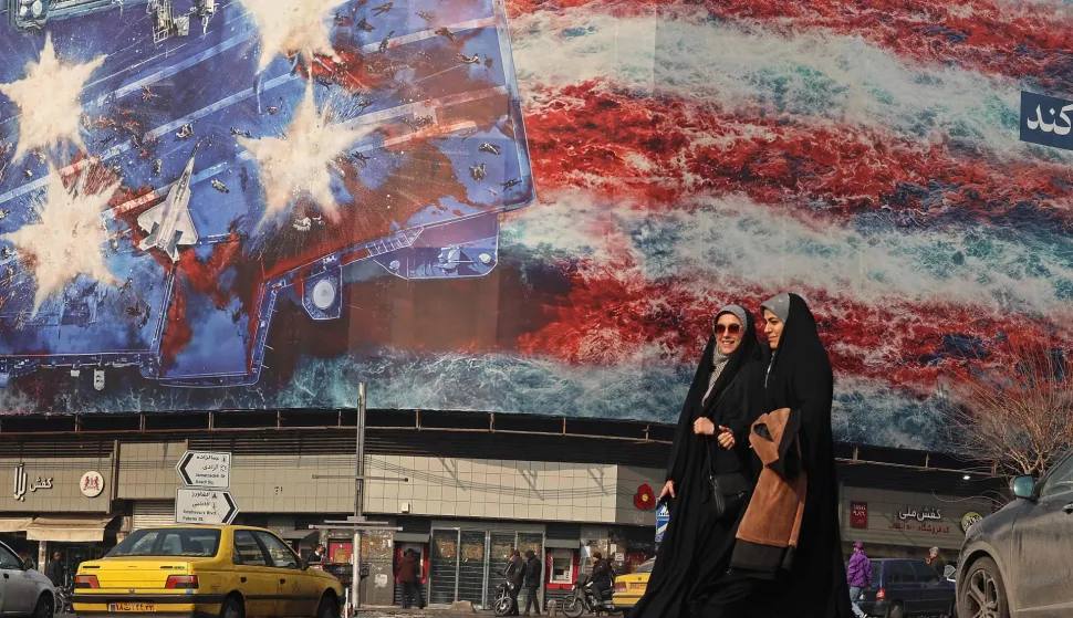 TOPSHOT - Iranian women walk past an anti-US billboard installed on a building at the Enqelab Square in Tehran on January 26, 2026. (Photo by ATTA KENARE/AFP)