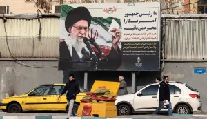 Iranians walk past a billboard showing Iranian supreme leader Ayatollah Ali Khamenei with anti-US rhetoric in Tehran on January 27, 2026. A US naval strike group led by an aircraft carrier has deployed to Middle Eastern waters, the United States said on January 26, 2026, as Tehran warned it was ready to hit back at any American attack launched in response to a crackdown on anti-government protests. (Photo by ATTA KENARE/AFP)