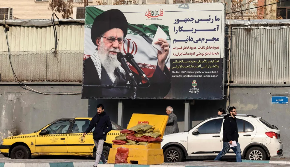 Iranians walk past a billboard showing Iranian supreme leader Ayatollah Ali Khamenei with anti-US rhetoric in Tehran on January 27, 2026. A US naval strike group led by an aircraft carrier has deployed to Middle Eastern waters, the United States said on January 26, 2026, as Tehran warned it was ready to hit back at any American attack launched in response to a crackdown on anti-government protests. (Photo by ATTA KENARE/AFP)