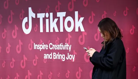 A woman uses her phone in front of Tiktok's booth during the World Economic Forum (WEF) annual meeting in Davos on January 19, 2026. The World Economic Forum takes place in Davos from January 19 to January 23, 2026. (Photo by INA FASSBENDER/AFP)