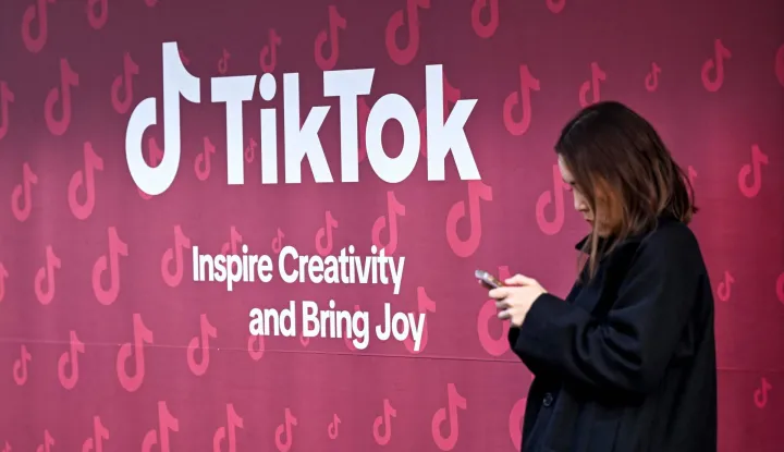 A woman uses her phone in front of Tiktok's booth during the World Economic Forum (WEF) annual meeting in Davos on January 19, 2026. The World Economic Forum takes place in Davos from January 19 to January 23, 2026. (Photo by INA FASSBENDER/AFP)