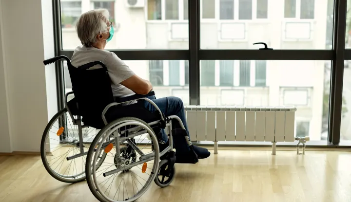 Pensive mature man in wheelchair wearing protective face mask while looking through the window during home quarantine.bolest invalidska kolica starost pacijent socijalna nakanada invalid ilustracija freepik