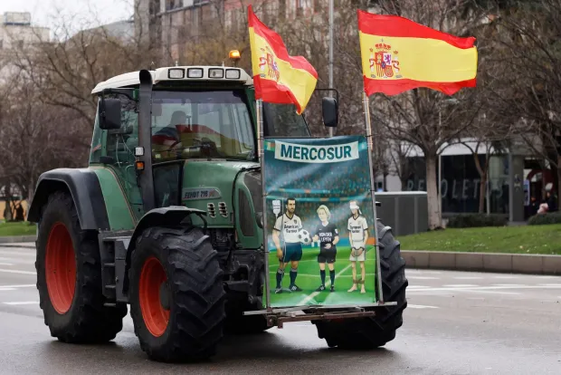 A poster placed on a tractor shows a caricature of European Commission President Ursula von der Leyen refereeing a football match between American and European farmers as Spanish farmers protest with tractors against EU-Mercosur trade deal and the economic pressures facing the agricultural sector, in Madrid on February 11, 2026. Spain on January 9, 2026 celebrated the approval by EU nations of a vast trade deal with South American bloc Mercosur, championed by business groups but loathed by many European farmers. (Photo by Oscar DEL POZO/AFP)